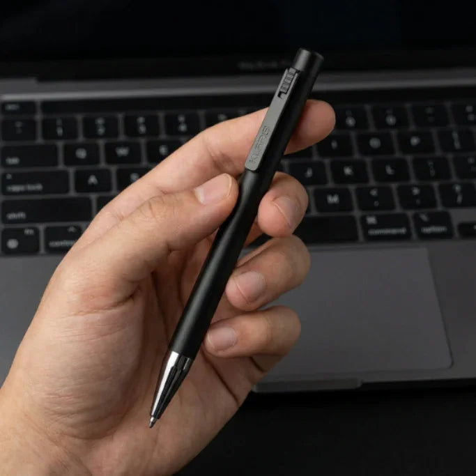 Hand holding a smart AI note-taking pen in front of a laptop keyboard.